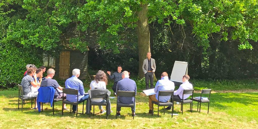 Group of professionals sitting in a circle outside under a tree.