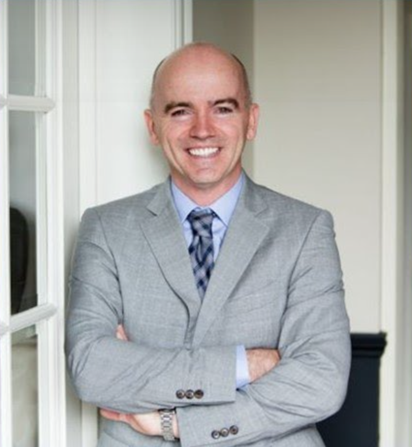 Photograph of Joe Drees, smiling, looking forward, wearing gray business suit with blue patterned tie and blue shirt