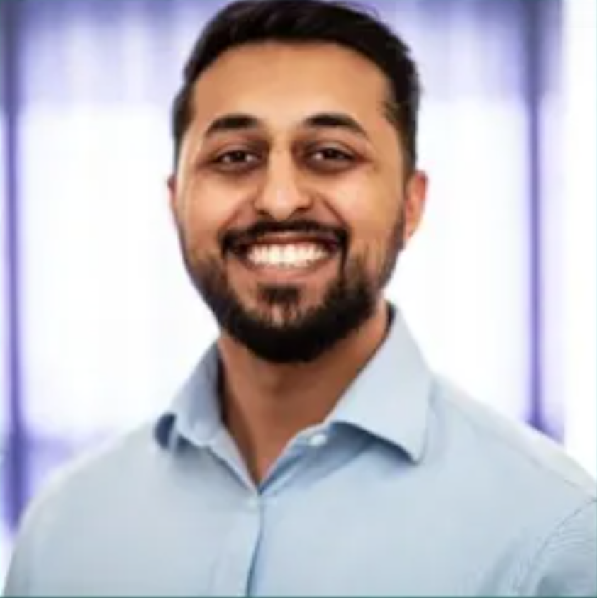 Photograph of Kris Amliwala, smiling, looking ahead at photographer, wearing light blue business shirt