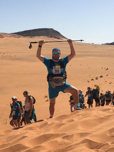 Athlete hiking in the Sahara, standing at top of a sand dune with arms over head
