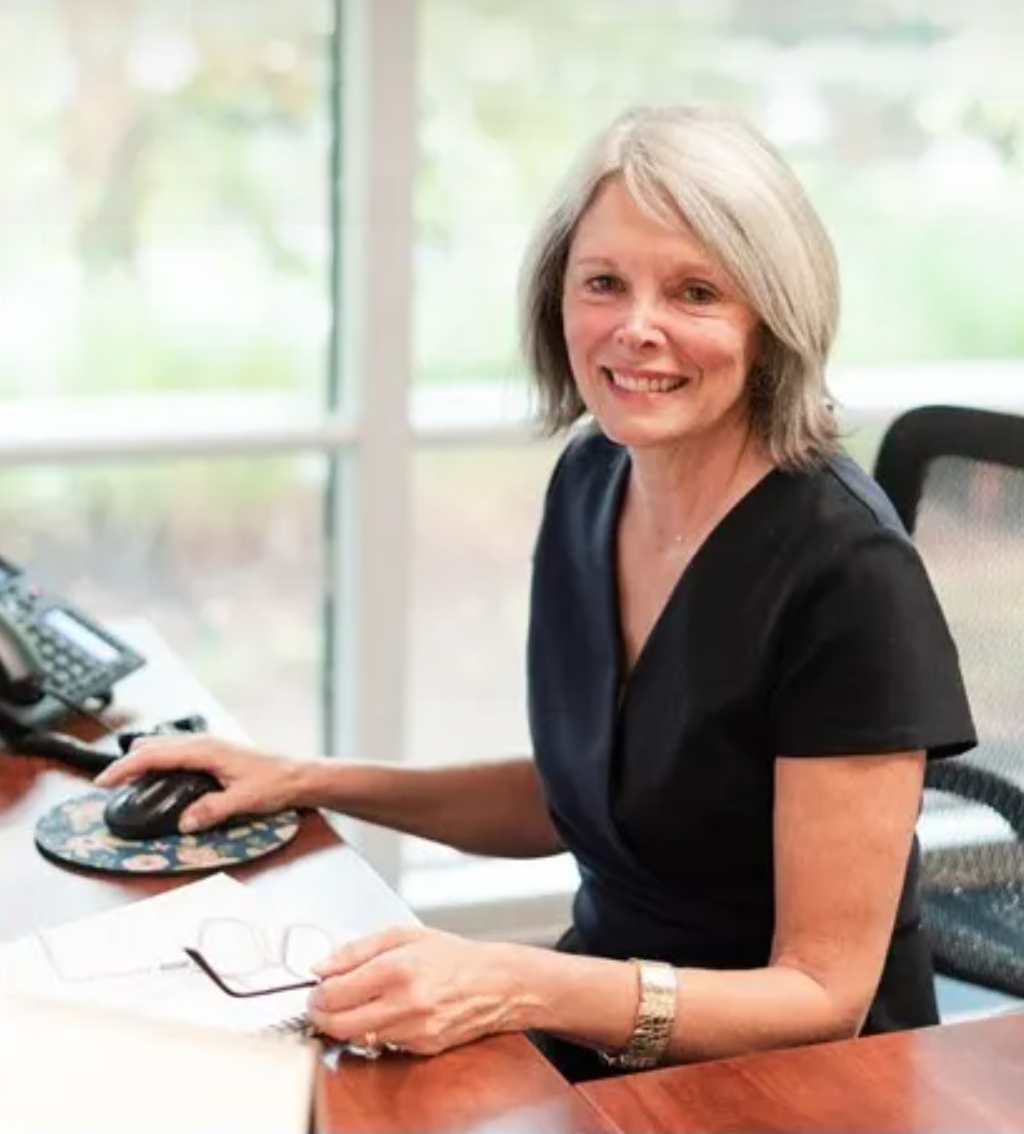 Photograph of Sarah Byrd, sitting at desk, smiling, looking at viewer, wearing black shirt