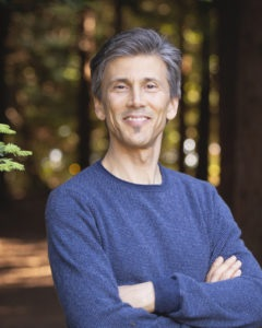 Photograph of Spencer Sherman, smiling with arms crossed, wearing blue crew neck shirt