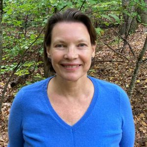 Photo of person wearing a blue v-neck shirt, standing outdoors and smiling toward camera.