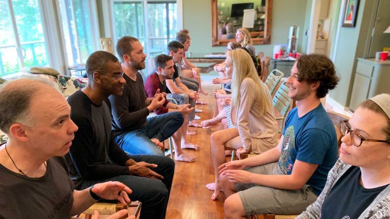 Group of adults sitting in two rows, facing each other, smiling, working on a client advisor role play.