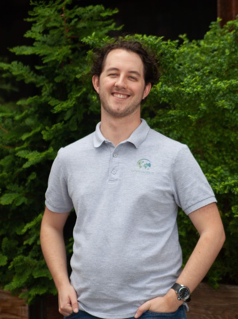 Man smiling in front of a green hedge