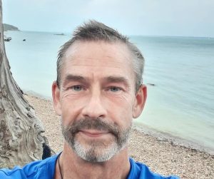 Man standing on a beach with the ocean behind him.