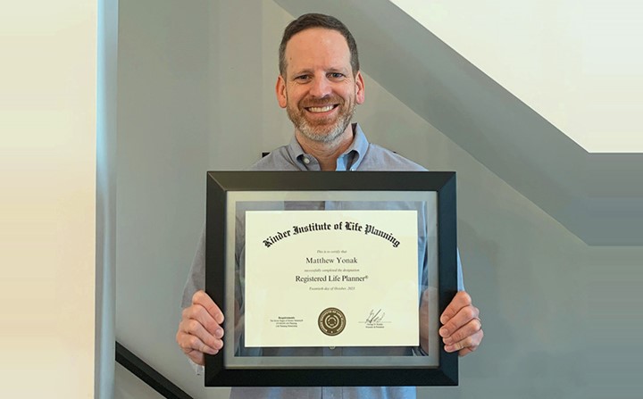 Matt Yonak, professional man in a collared shirt, smiles while holding a framed certificate.